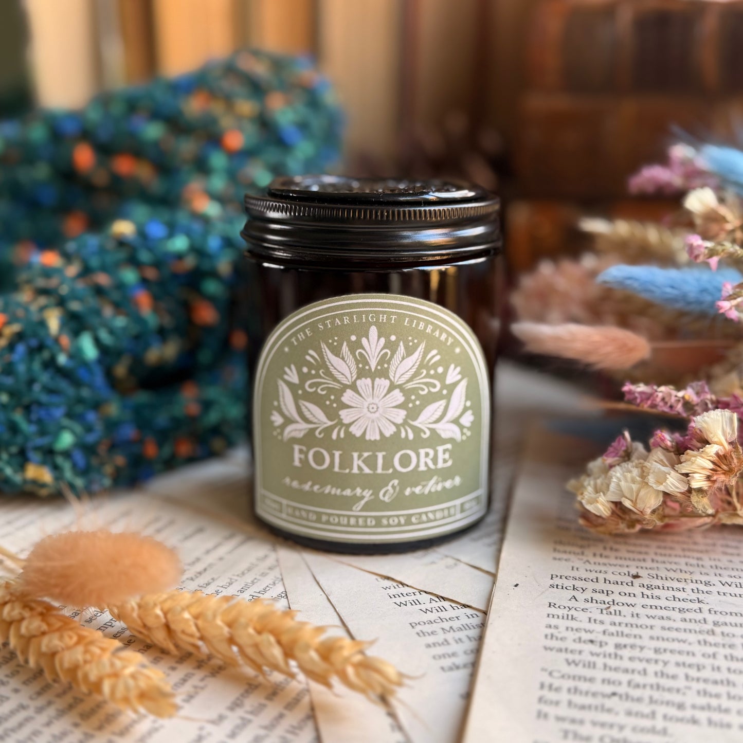 Folklore bookish candle, surrounded by books, knits and dried flowers