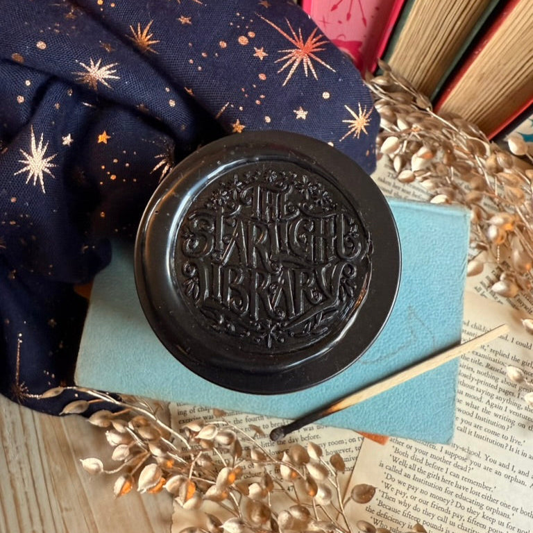 Black wax stamp, featuring The Starlight Library logo on the lid of a bookish candle.